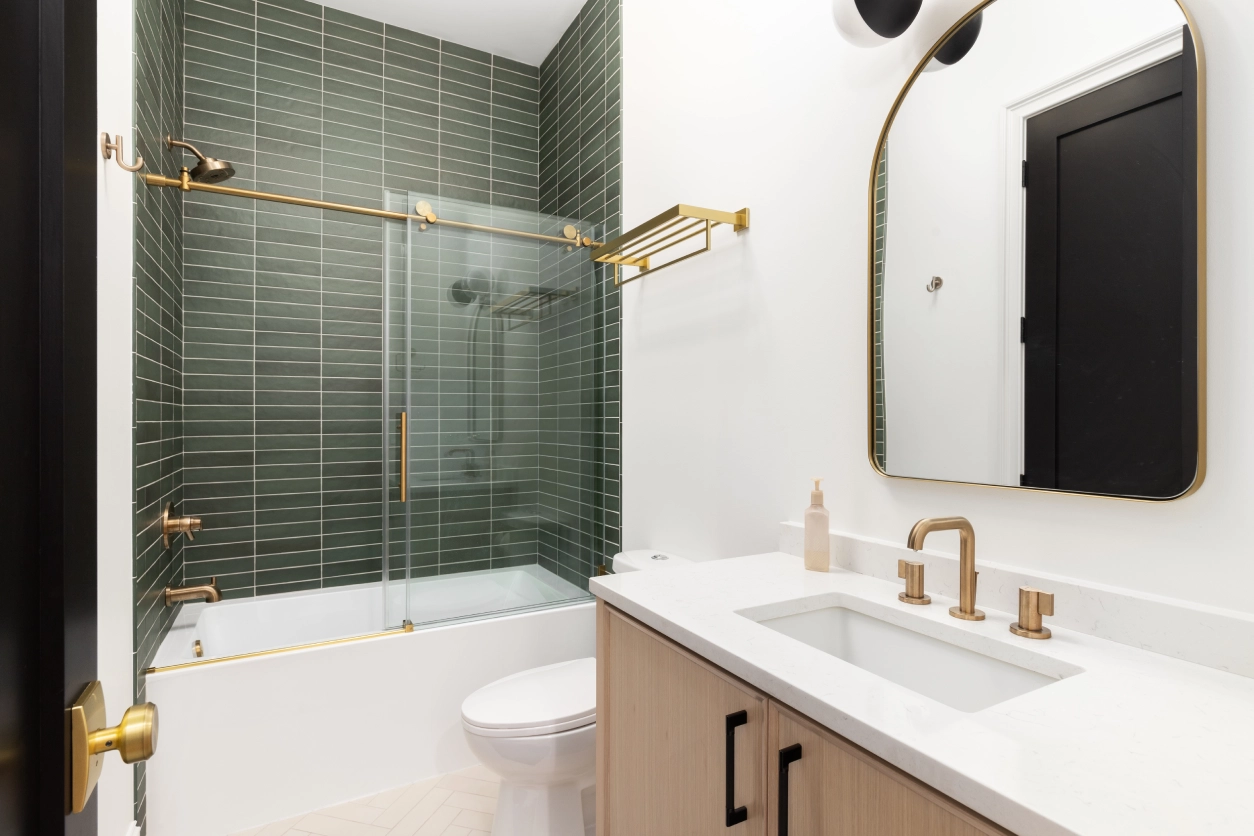 Modern bathroom with green tile and gold fixtures.