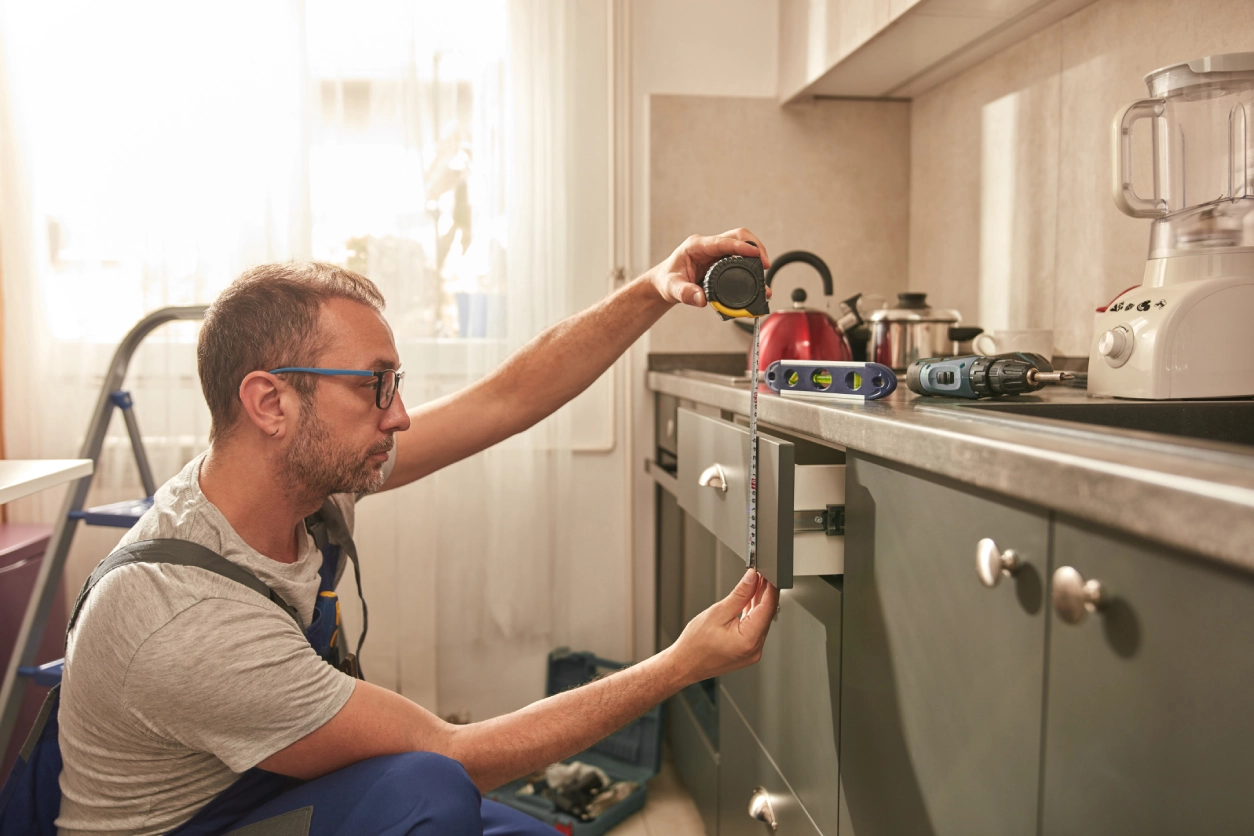 Man measuring kitchen cabinet with tape measure.